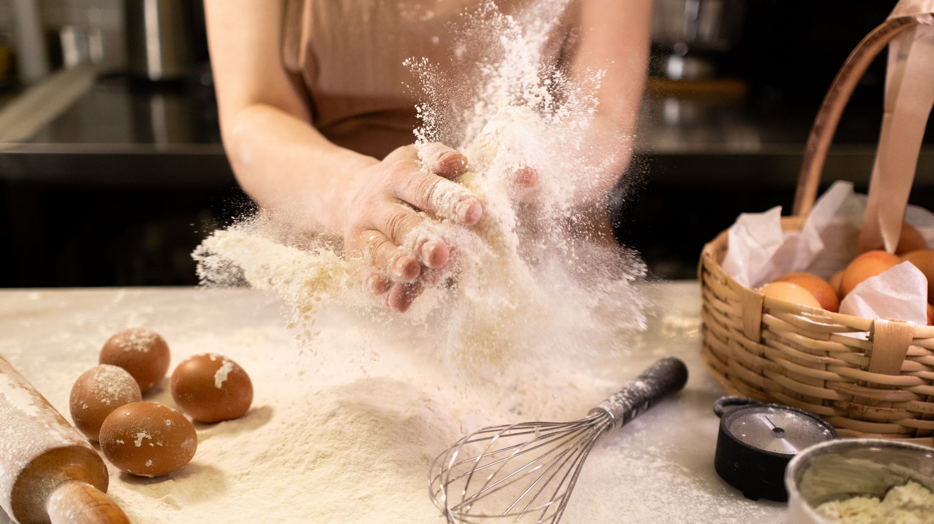 Œufs bruns dans un panier en osier, sur un plan de travail fariné avec un fouet et un rouleau à pâtisserie